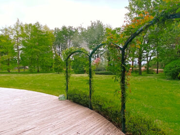 Archi da giardino in metallo decorati da rose rampicanti, con diffusione visibile del sistema antizanzare nebulizzato in un ampio parco verde privato.