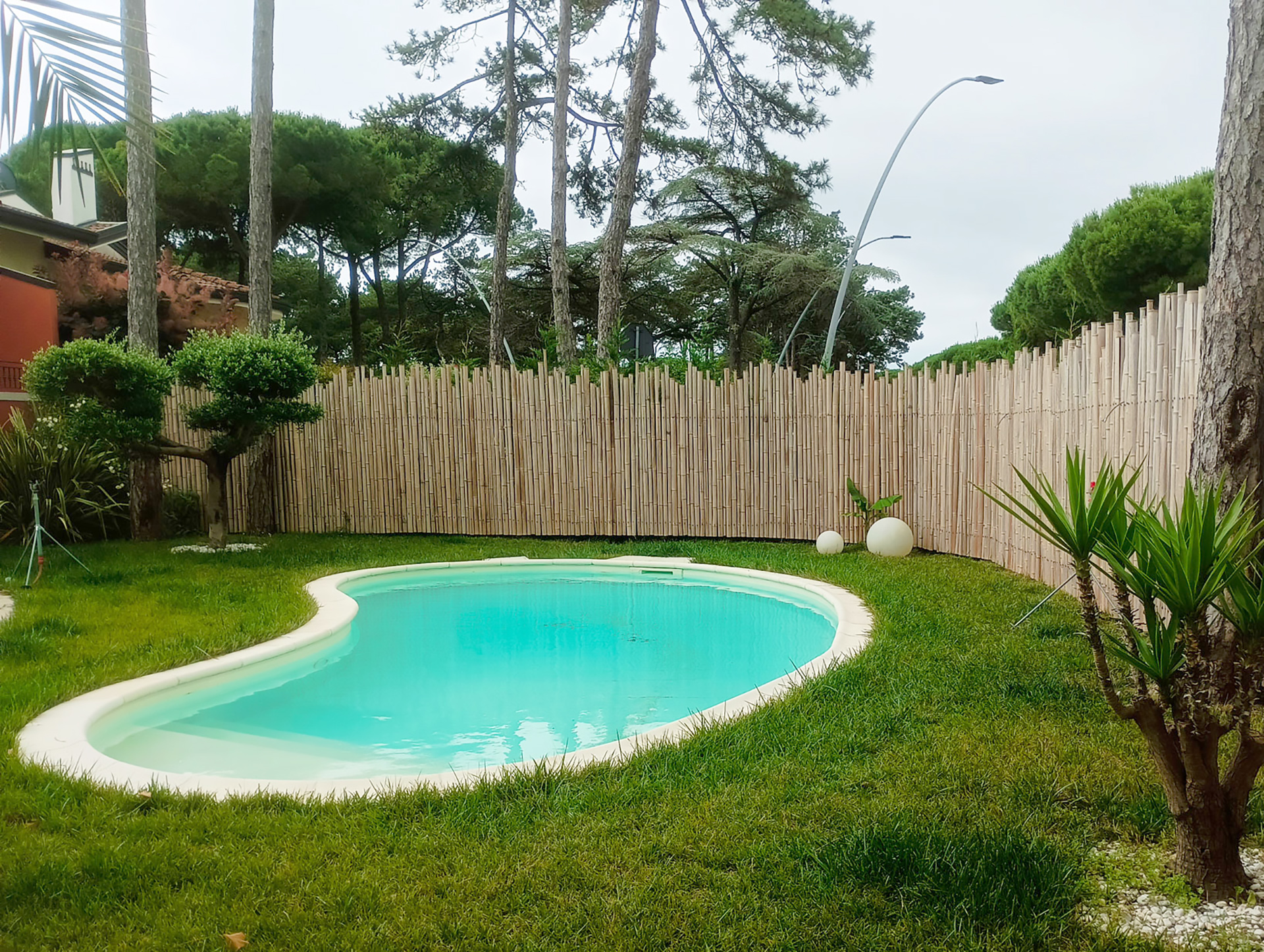 Piscina privata in giardino con erba curata e recinzione in bambù, ambientazione ideale per l’uso di sistemi antizanzare da esterno.